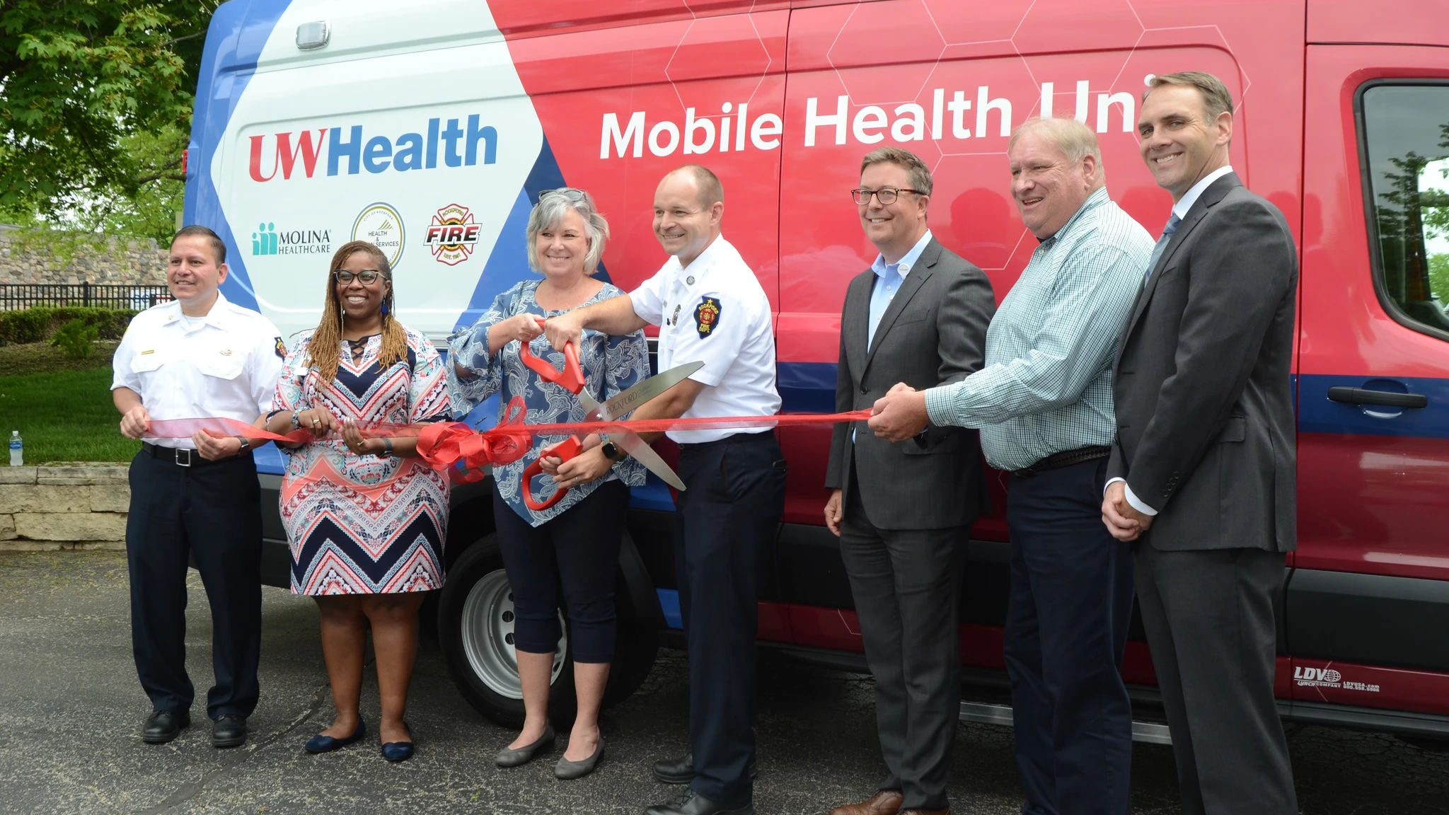 Seven people in front of Mobile Health Unit at ribbon cutting.