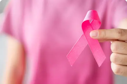 Woman in pink shirt holding Breast Cancer Awareness Month pink ribbon.