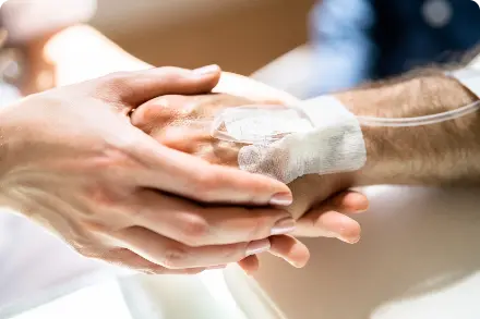 Health care worker holding the hand of a patient who has IV in his hand.