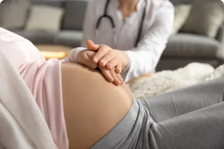 Pregnant woman with hand on stomach and health care provider with hand on woman's hand.