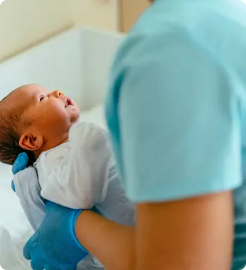 Newborn baby looking up at nurse holding him.