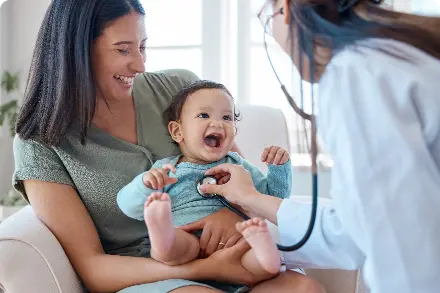 Mom holding laughing baby while physician listens to baby's heart.