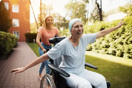 Cancer patient in wheel chair, smiling as another woman pushes her.